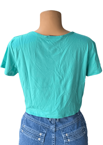 Vista de espalda. Blusa corta verde con diseño amarrado en la parte delantera y detalles de tirantes cruzados en el escote.