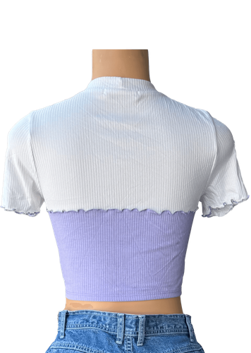 Vista de espalda. Blusa corta bicolor con parte superior blanca y parte inferior morada, detalles ondulados en el borde.