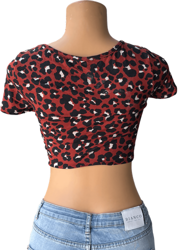 Vista de espalda. Blusa corta con estampado de leopardo marrón y detalle anudado al frente.