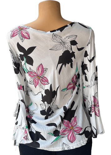 Vista de espalda (dos de dos). Una blusa blanca de manga larga con un estampado de flores en tonos negros, rosas y verdes.