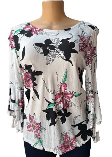 Vista de frente (dos de dos). Una blusa blanca de manga larga con un estampado de flores en tonos negros, rosas y verdes.