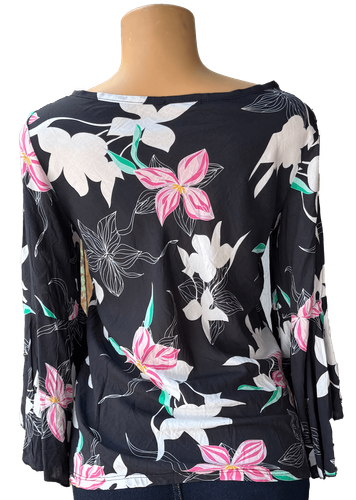 Vista de espalda (dos de dos). Una blusa negra de manga larga con un estampado de flores en tonos blancos, rosas y verdes.