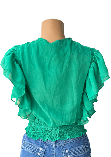Vista de espalda. Una blusa verde con volantes y detalles fruncidos en la cintura, y un lazo en el escote.