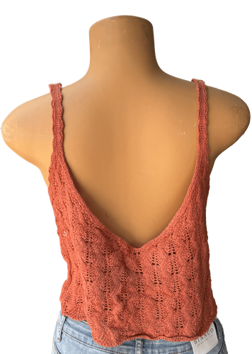 Vista de espalda. Un top de punto grueso color salmón, sin mangas y con escote pronunciado en la espalda.