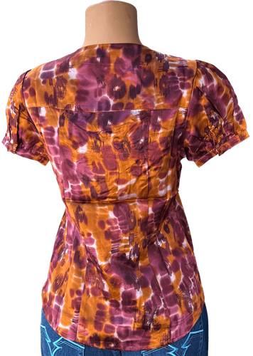 Vista de espalda (una de dos). Blusa de manga corta con estampado tie-dye en tonos púrpura y naranja.
