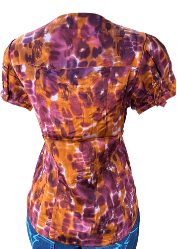 Vista de espalda (dos de dos). Blusa de manga corta con estampado tie-dye en tonos púrpura y naranja.