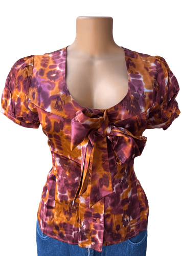 Vista de frente (dos de dos). Blusa de manga corta con estampado tie-dye en tonos púrpura y naranja.