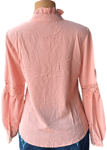 Vista de espalda (una de dos). Una blusa salmón de manga larga con detalles de encaje en las mangas y un lazo decorativo en el cuello.