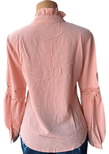 Vista de espalda (dos de dos). Una blusa salmón de manga larga con detalles de encaje en las mangas y un lazo decorativo en el cuello.