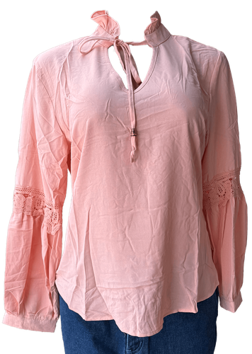 Vista de frente (dos de dos). Una blusa salmón de manga larga con detalles de encaje en las mangas y un lazo decorativo en el cuello.