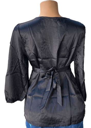 Vista de espalda (dos de dos). Una blusa negra simple con mangas largas y un cinturón ajustable en la cintura.