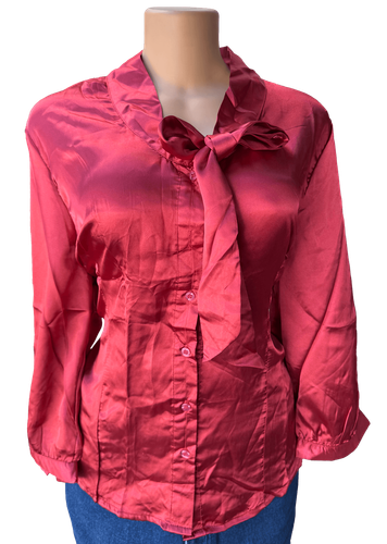 Vista de frente (dos de dos). Blusa de satén con mangas largas y un diseño clásico de botones en la parte frontal y un lazo decorativo en el cuello.