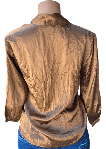 Vista de espalda (una de dos).  Blusa dorada con botones y lazo al cuello, manga larga.