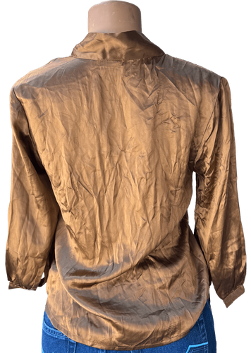 Vista de espalda (dos de dos).  Blusa dorada con botones y lazo al cuello, manga larga.