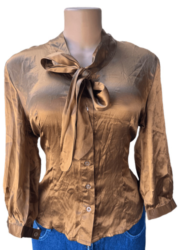 Vista de espalda (dos de dos).  Blusa dorada con botones y lazo al cuello, manga larga.