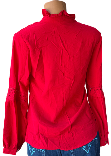 Vista de espalda (una de dos). Blusa roja vibrante con cuello alto y diseño de encaje en las mangas, cierre de lazo en el cuello y detalle de volantes.