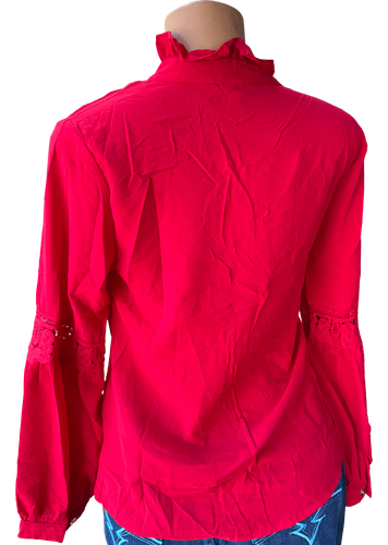 Vista de espalda (dos de dos). Blusa roja vibrante con cuello alto y diseño de encaje en las mangas, cierre de lazo en el cuello y detalle de volantes.