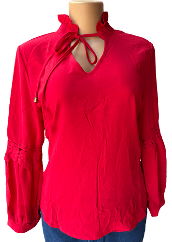 Vista de frente (dos de dos). Blusa roja vibrante con cuello alto y diseño de encaje en las mangas, cierre de lazo en el cuello y detalle de volantes.